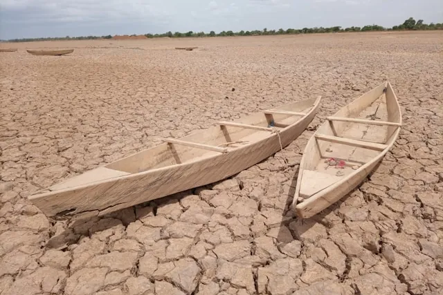 Trockener See, auf dem zwei Boote liegen, Symbol für den Klimawandel